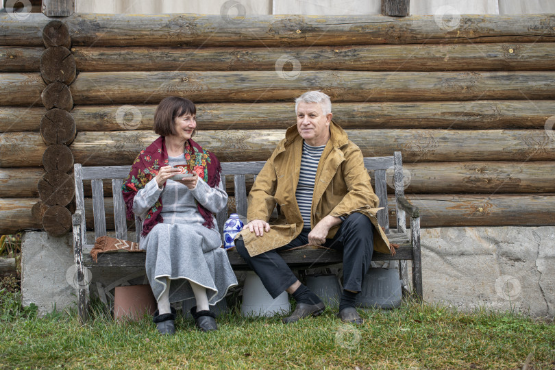 Скачать Деревенские пенсионеры сидят на скамейке возле бревенчатой бани. фотосток Ozero