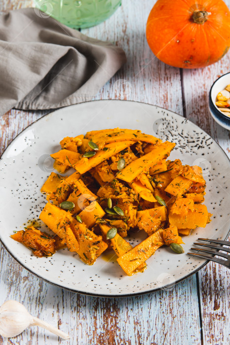 Скачать Запеченные ломтики тыквы с чесноком и укропом на тарелке на столе, вид сверху фотосток Ozero