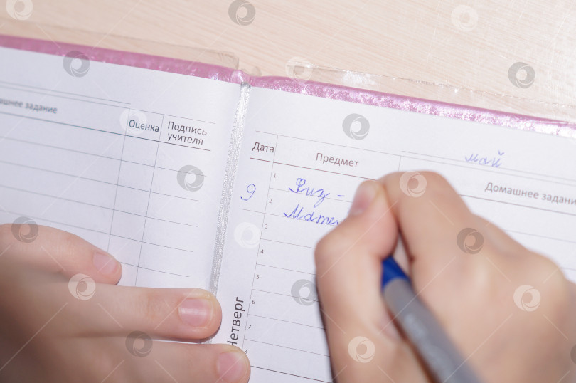 Скачать Школьник заполняет дневник, пишет месяц, число и названия предметов синей ручкой фотосток Ozero