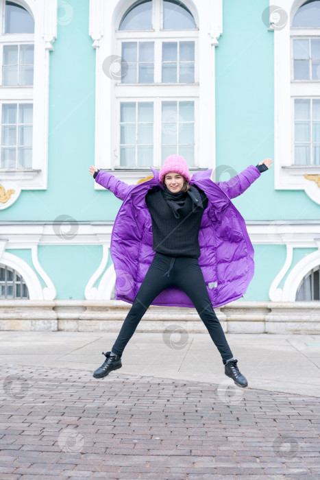Скачать Женщина в фиолетовом пальто и черных брюках подпрыгивает в воздух фотосток Ozero