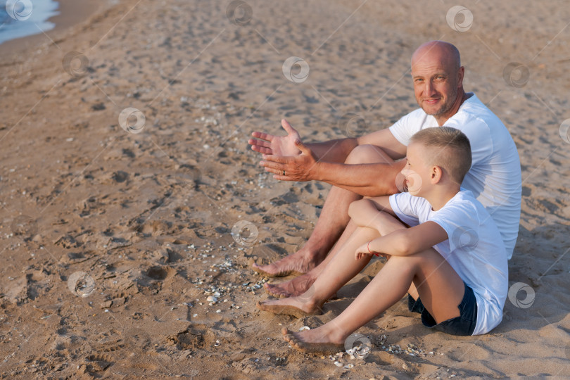 Скачать Мужчина и мальчик сидят на пляже фотосток Ozero