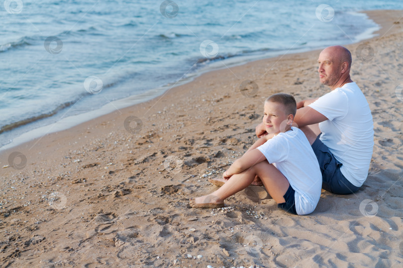 Скачать Мужчина и мальчик сидят на пляже фотосток Ozero