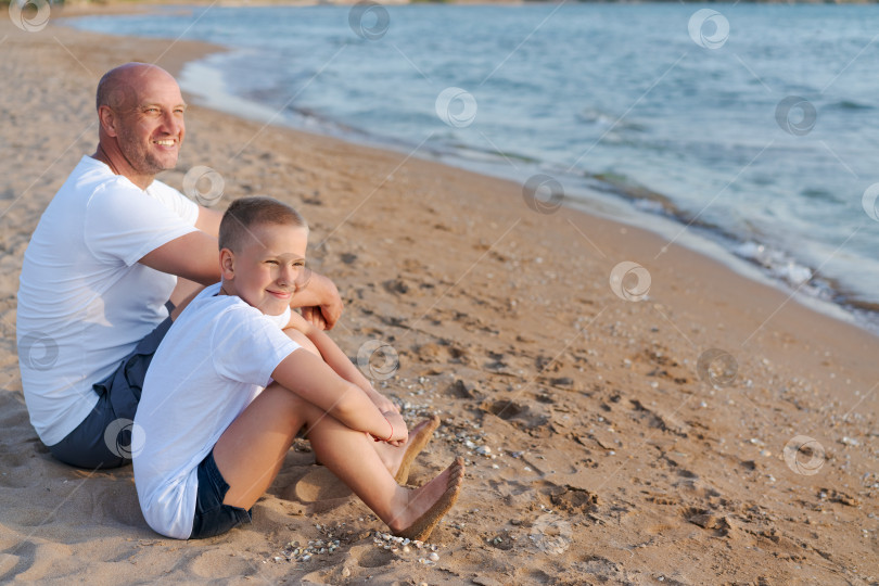 Скачать Мужчина и мальчик сидят на пляже фотосток Ozero
