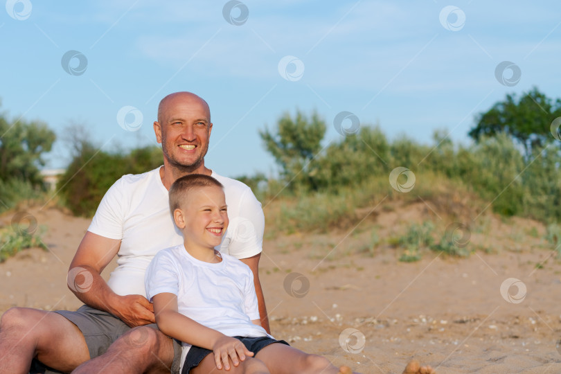 Скачать Мужчина и мальчик сидят на пляже фотосток Ozero