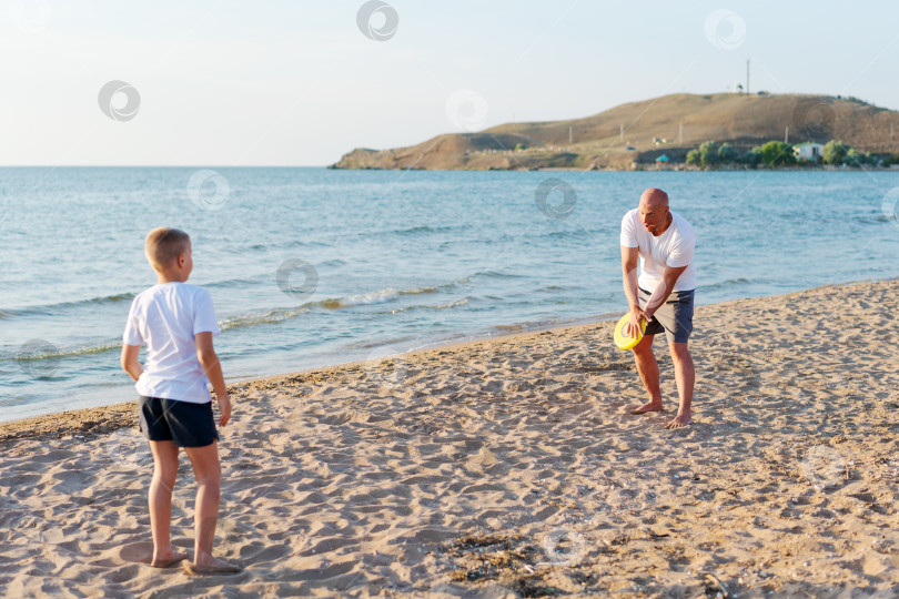 Скачать Мужчина и мальчик играют во фрисби на пляже фотосток Ozero