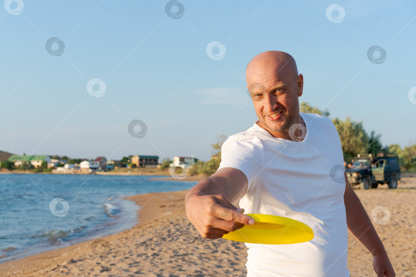 Скачать Мужчина стоит на пляже и держит в руках желтую летающую тарелку фотосток Ozero