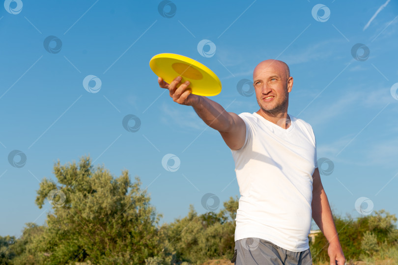 Скачать Мужчина держит в руке желтую летающую тарелку-фрисби фотосток Ozero