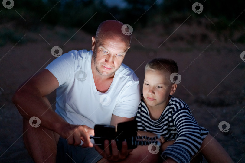 Скачать Мужчина и мальчик сидят на земле и смотрят в сотовый телефон фотосток Ozero