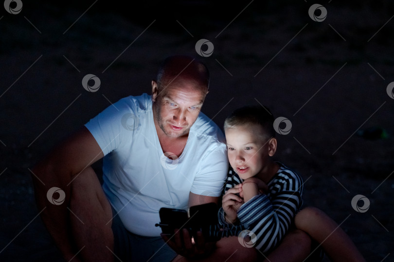 Скачать Мужчина и мальчик сидят на земле и смотрят в сотовый телефон фотосток Ozero