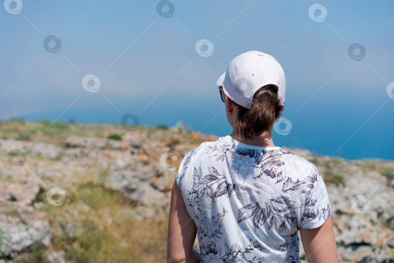 Скачать Женщина в белой шляпе и белой рубашке стоит на скалистом холме фотосток Ozero