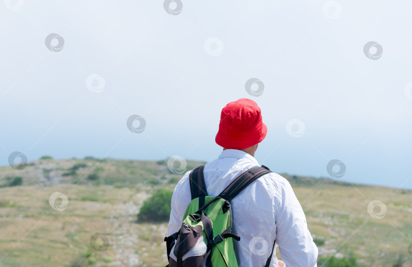 Скачать Человек в красной шляпе и зеленом рюкзаке стоит на холме фотосток Ozero