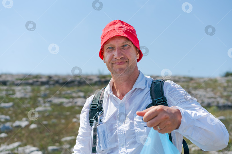 Скачать Мужчина в красной шляпе и белой рубашке держит в руках пластиковый пакет фотосток Ozero