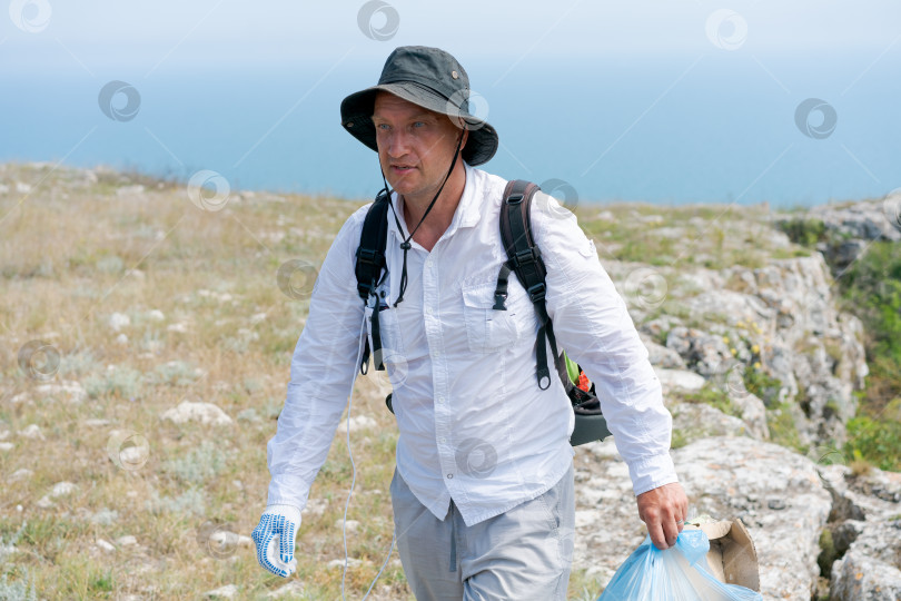 Скачать Мужчина в белой рубашке и шляпе идет по каменистому склону холма фотосток Ozero