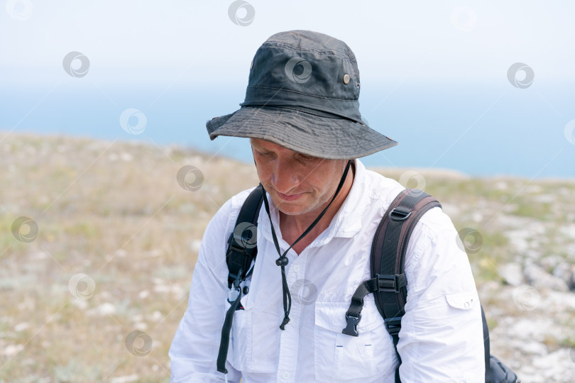 Скачать Мужчина в черной шляпе и белой рубашке сидит на холме фотосток Ozero