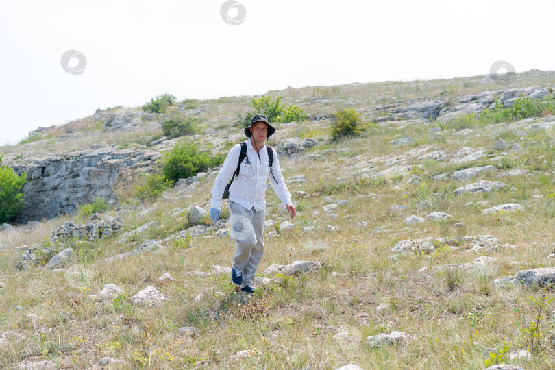 Скачать Мужчина идет по склону холма с рюкзаком фотосток Ozero