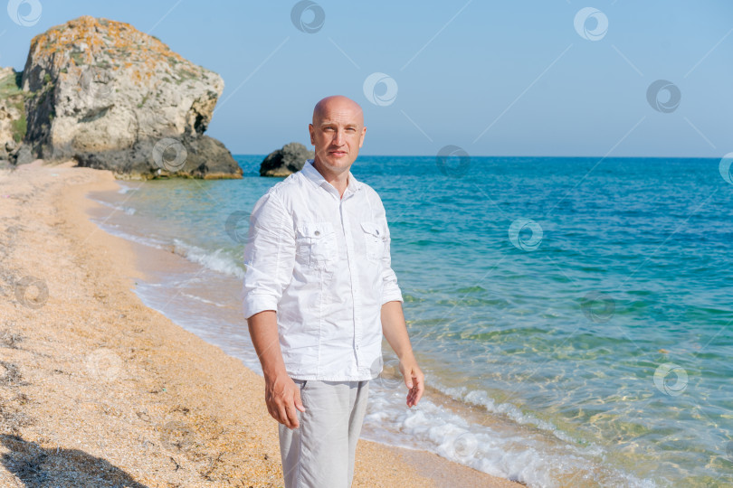 Скачать Мужчина стоит на пляже, на заднем плане видна скала фотосток Ozero