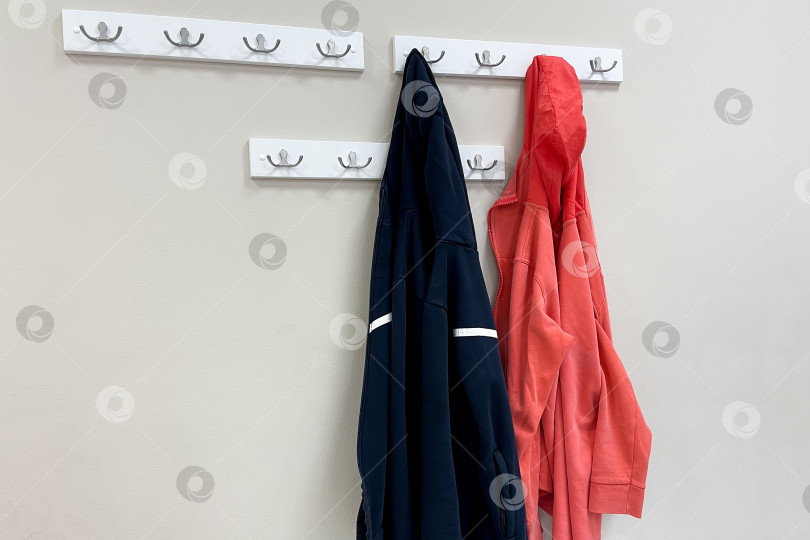 Скачать Осенняя верхняя одежда, куртка и пальто на вешалках на деревянной полке гардероба в прихожей фотосток Ozero