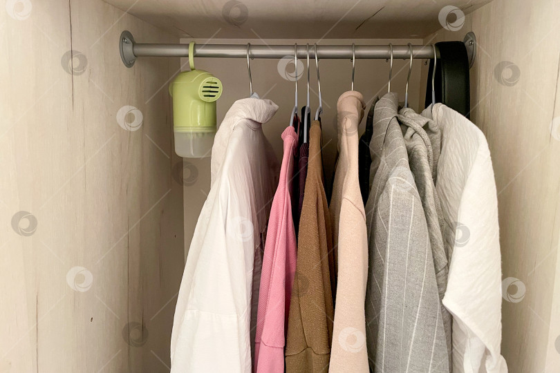 Скачать Портативный осушитель воздуха висит в шкафу вместе с одеждой рубашками и джемперами фотосток Ozero