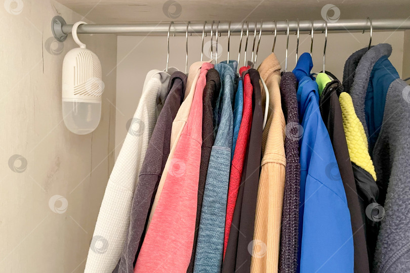 Скачать Портативный осушитель воздуха висит в шкафу вместе с одеждой рубашками и джемперами фотосток Ozero