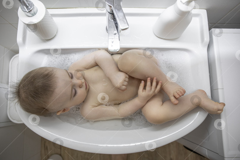 Скачать Маленькая девочка лежит в раковине в ванной фотосток Ozero