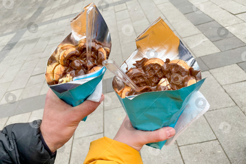 Скачать Воздушная бельгийская вафля с шоколадной пастой в рожке, пара держит десерт в руках фотосток Ozero