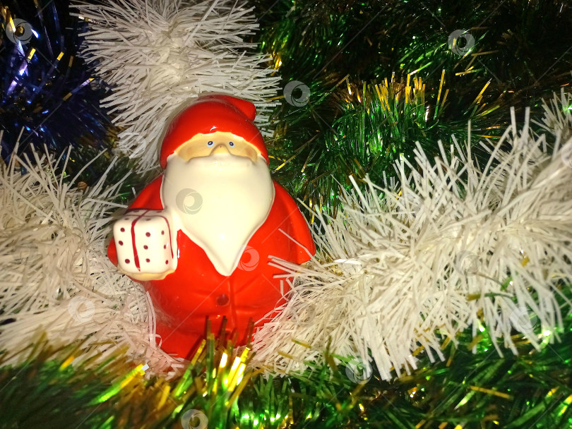 Скачать Фигурка Деда Мороза на фоне разноцветной мишуры фотосток Ozero