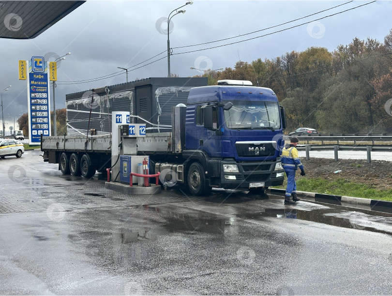 Скачать Заправщик обслуживает грузовик на автозаправочной станции в дождливую погоду фотосток Ozero