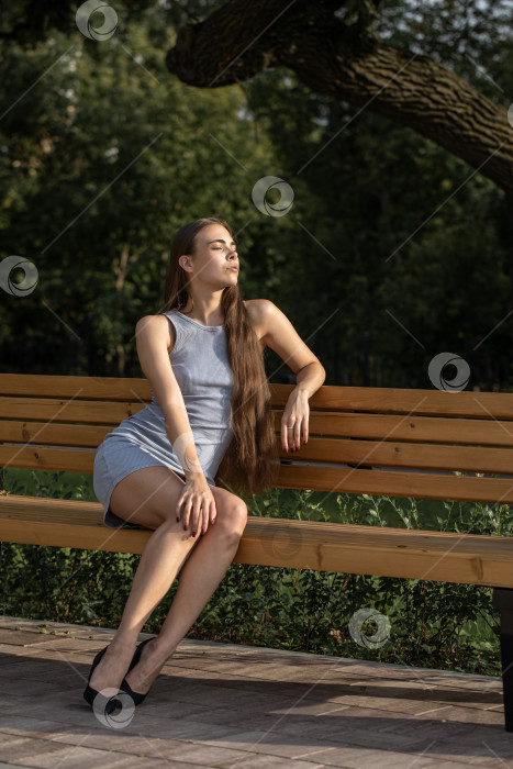 Скачать Молодая красивая женщина сидит на скамейке в летнем парке фотосток Ozero