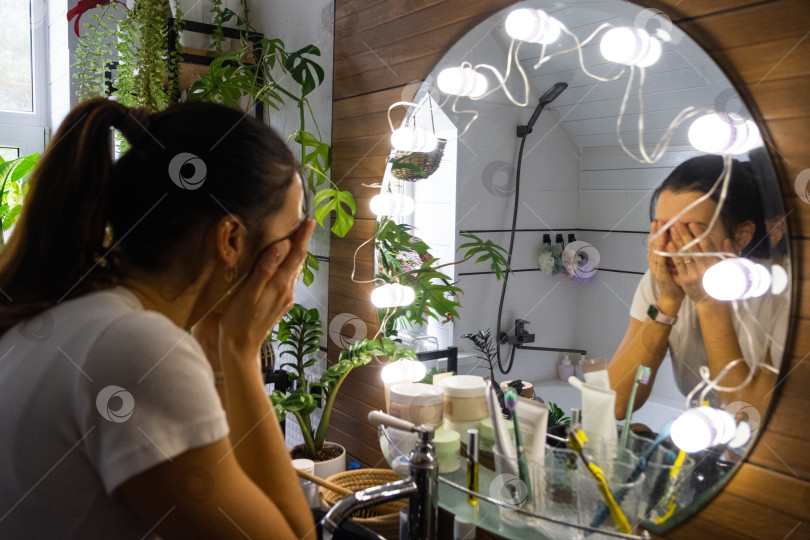 Скачать Женщина умывается в ванной и смотрится в зеркало с подсветкой. Утренняя и вечерняя гигиена фотосток Ozero