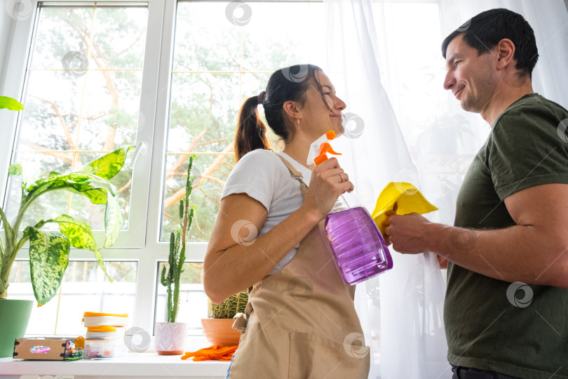 Скачать Муж помогает своей жене вручную мыть окна в доме с помощью тряпки для мытья посуды и швабры внутри помещений. Наведение порядка и чистоты, услуги по уборке фотосток Ozero