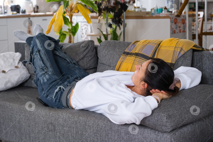 Скачать Женщина дома в белом интерьере лежит на диване и смотрит телевизор. Домашний отдых, досуг фотосток Ozero