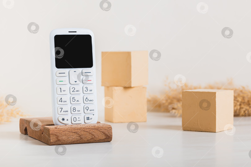 Скачать Модный белый кнопочный телефон в стиле ретро на деревянной подставке на столе фотосток Ozero