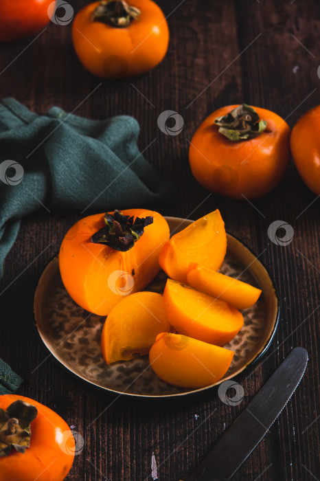 Скачать Кусочки и половинки плодов хурмы на тарелке и на столе в вертикальном положении фотосток Ozero