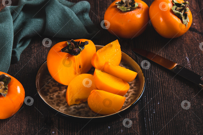 Скачать Кусочки и половинки плодов хурмы на тарелке и на столе фотосток Ozero