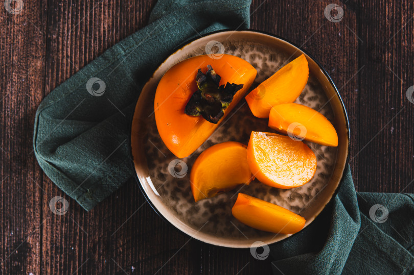 Скачать Крупный план свежей спелой нарезанной хурмы на тарелке, стоящей на столе, вид сверху фотосток Ozero