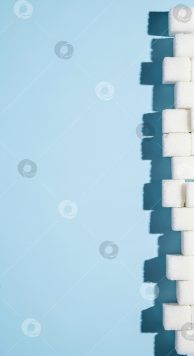 Скачать Белые кубики сахара на синем фоне, вертикальный шаблон для сладких блюд, связанных с сахарным диабетом и концепциями здорового питания, с пространством для копирования текста. фотосток Ozero