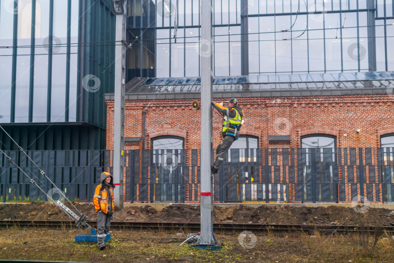 Скачать Рабочие устанавливают систему оповещения на столбе на железной дороге на фоне промышленных зданий. фотосток Ozero
