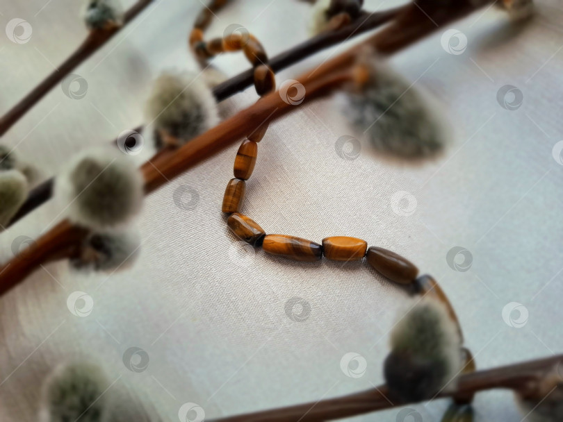 Скачать Нить натурального камня "тигровый глаз" и веточки вербы на сером шелковом фоне. фотосток Ozero