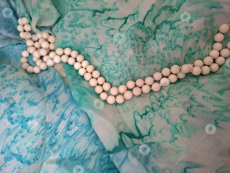 Скачать Нить белого натурального агата на шелковой ткани салатового, бирюзового тонов. фотосток Ozero