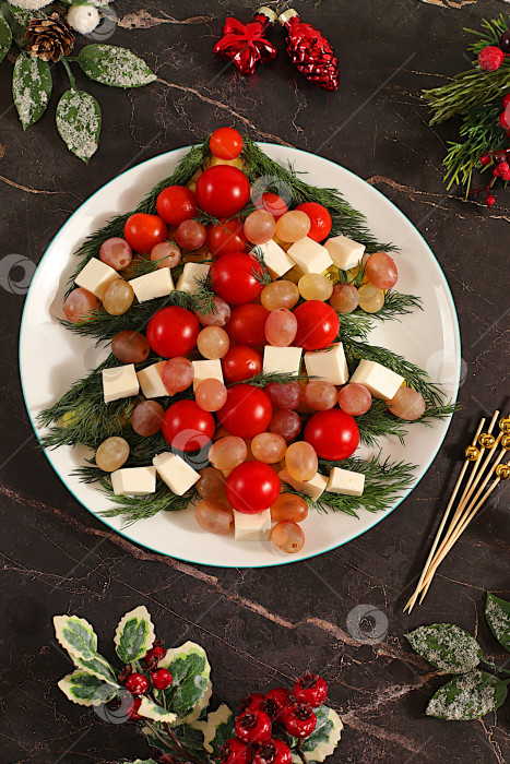 Скачать Рождественские и новогодние блюда, традиционный праздничный салат в виде живой съедобной елки с сыром фета, оливками, помидорами и виноградом, еловыми ветками и украшениями, идея кулинарного дизайна фотосток Ozero
