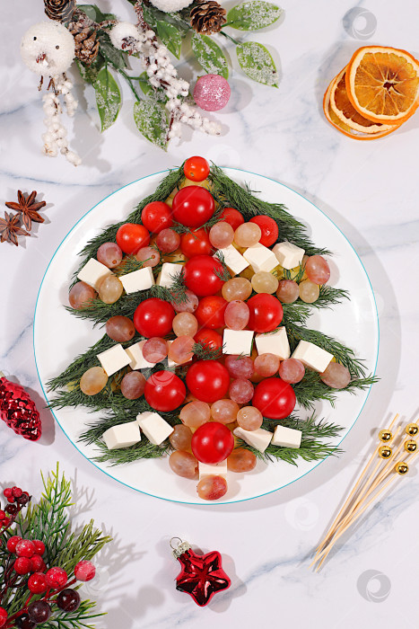 Скачать Традиционный праздничный салат в виде живой съедобной елки с сыром фета, оливками, помидорами и виноградом, рождественские и новогодние блюда, идея оформления блюд, еловые ветки и украшения фотосток Ozero