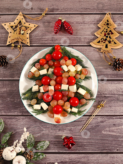 Скачать Рождественские и новогодние блюда, традиционный праздничный салат в виде живой съедобной елки с сыром фета, оливками, помидорами и виноградом, еловыми ветками и украшениями, идея кулинарного дизайна фотосток Ozero
