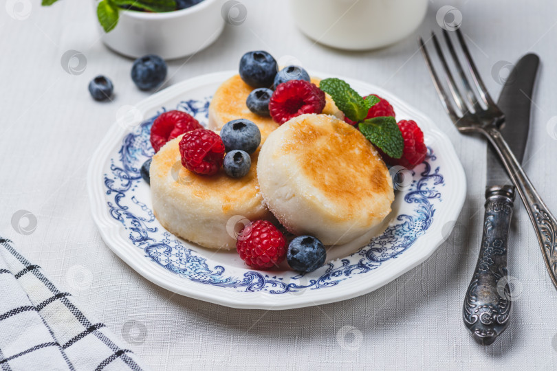 Скачать Сырники с сахарной пудрой и ягодами на тарелке фотосток Ozero