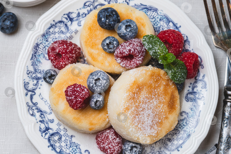Скачать Сырники с сахарной пудрой и ягодами на тарелке фотосток Ozero