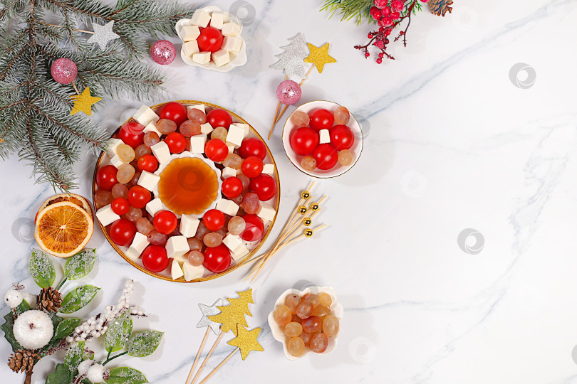 Скачать Праздничный новогодний салат с сыром фета, помидорами, виноградом, оливками и медом с еловыми ветками и украшениями, идея оформления блюда, рождественские и новогодние блюда, шаблон меню и баннер для ресторана фотосток Ozero