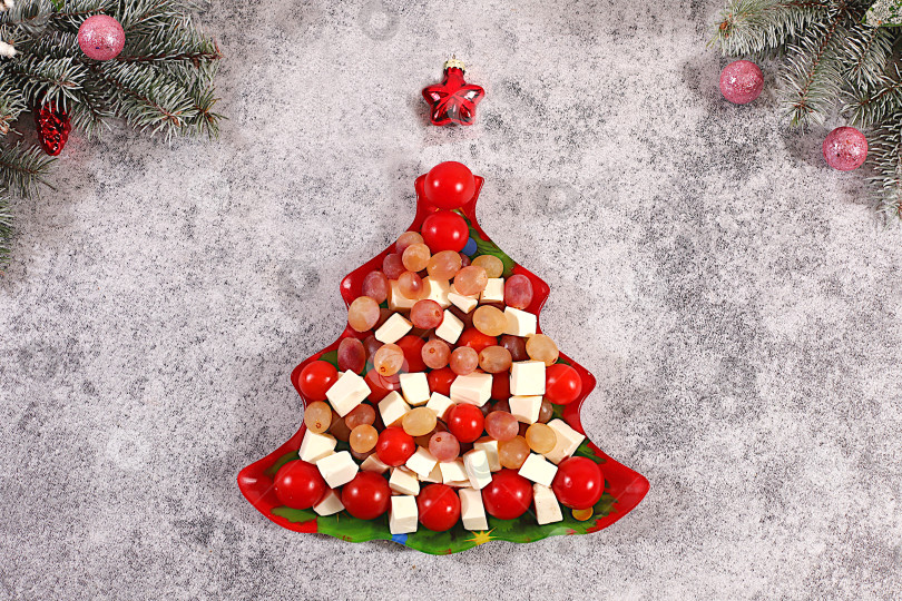 Скачать Традиционный праздничный салат в форме рождественской елки с сыром фета, помидорами, виноградом, оливками и медом, украшенный еловыми ветками и другими украшениями, идея оформления блюда, рождественские и новогодние блюда, шаблон меню ресторана и баннер фотосток Ozero