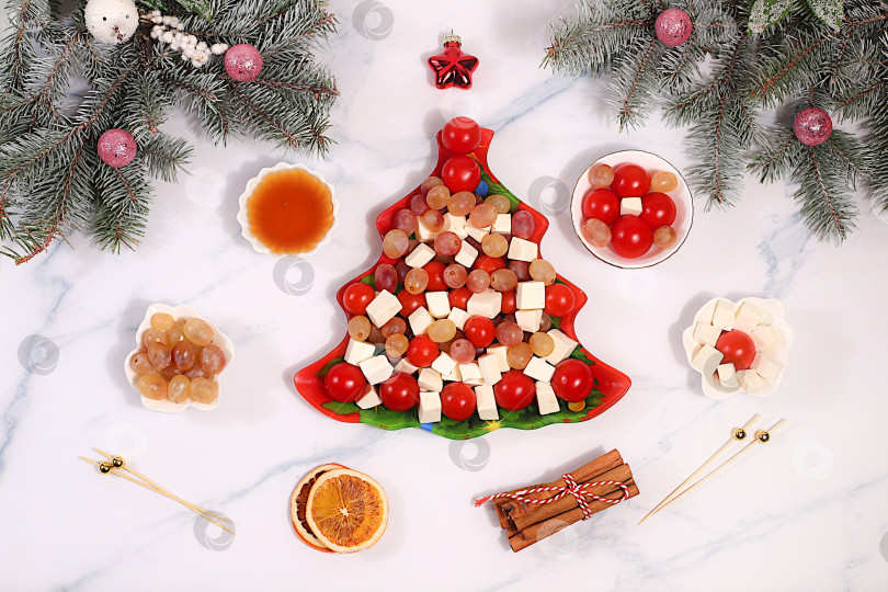 Скачать Праздничный новогодний салат в форме елочки с сыром фета, помидорами, виноградом, оливками и медом, украшенный еловыми ветками и другими украшениями. Идея оформления блюда. Рождественские и новогодние блюда, шаблон меню и баннер ресторана. фотосток Ozero