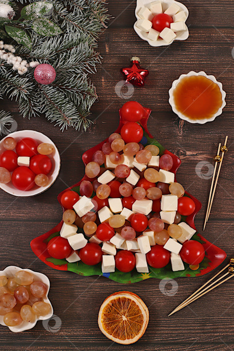 Скачать Традиционный праздничный салат в форме рождественской елки с сыром фета, помидорами, виноградом, оливками и медом, украшенный еловыми ветками и другими украшениями, идея оформления блюда, рождественские и новогодние блюда, шаблон меню ресторана и баннер фотосток Ozero