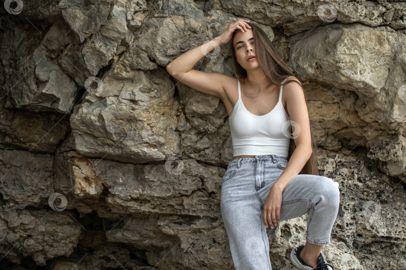 Скачать Красивая женщина в белом топе и серых джинсах позирует на скалах в горах фотосток Ozero