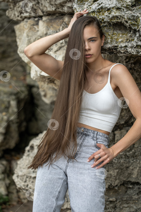 Скачать Красивая женщина в белом топе и серых джинсах позирует на скалах в горах фотосток Ozero